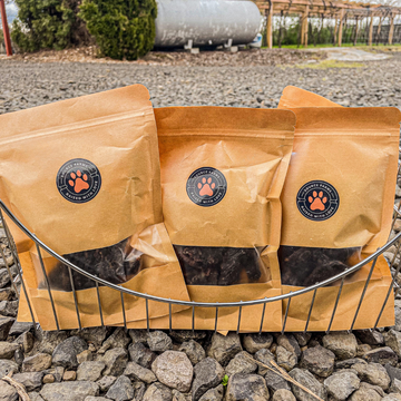 Image of 3 bags of dog treats displayed in a metal basket on gravel road