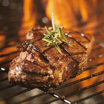 image of a steak on a hot grill with rosemary sprig on top