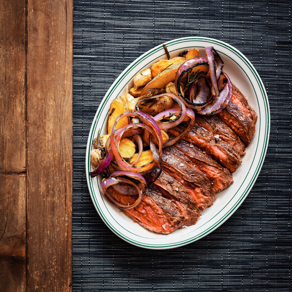 image of cooked Bavette steak with red onions and fingerling potatoes on a platter