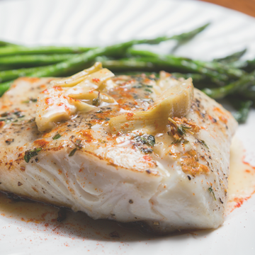 image of a fillet of halibut on a white plate with green beans in background