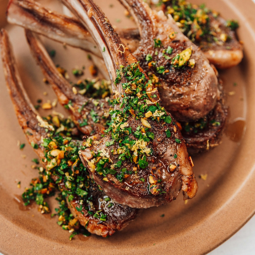 image of cooked lamb rib chops with pistachio gremolata on top on a copper colored plate