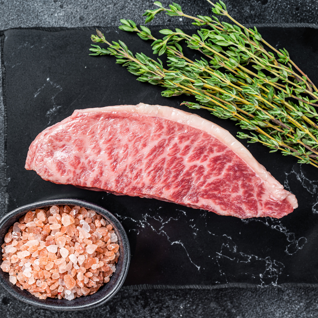 Image of a raw wagyu steak on a board with rosemary sprigs and pink salt on the sides